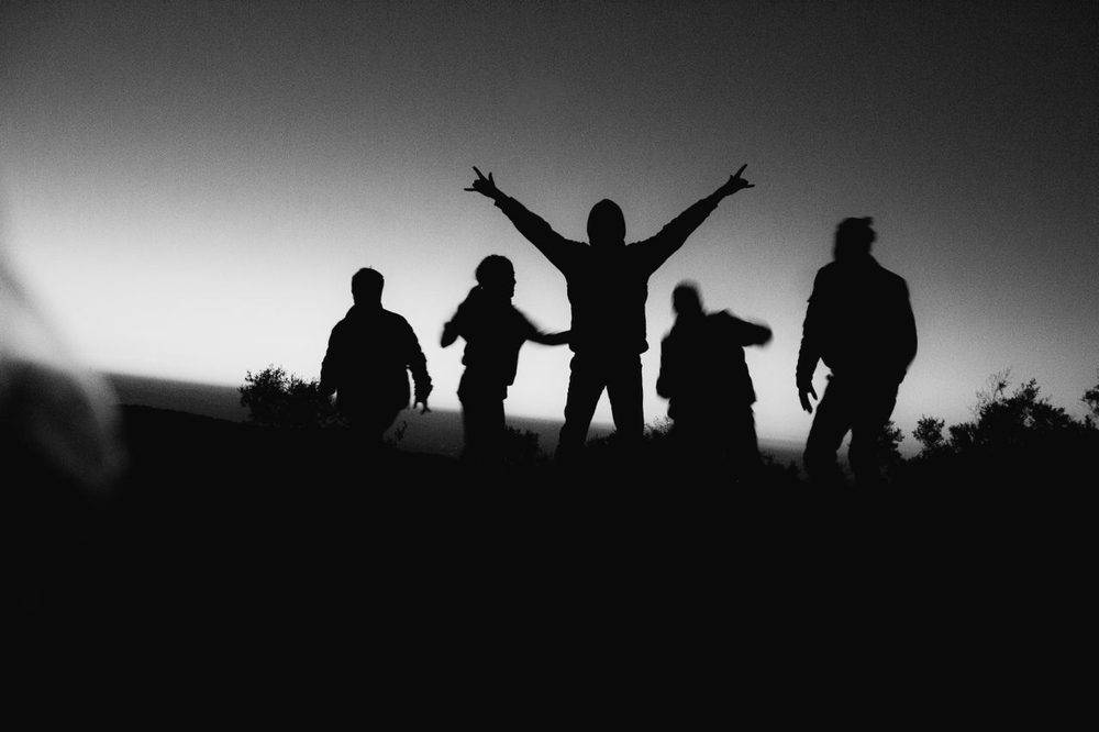 Siluetas de un grupo de personas en un alto, recortadas contra el cielo del atardecer